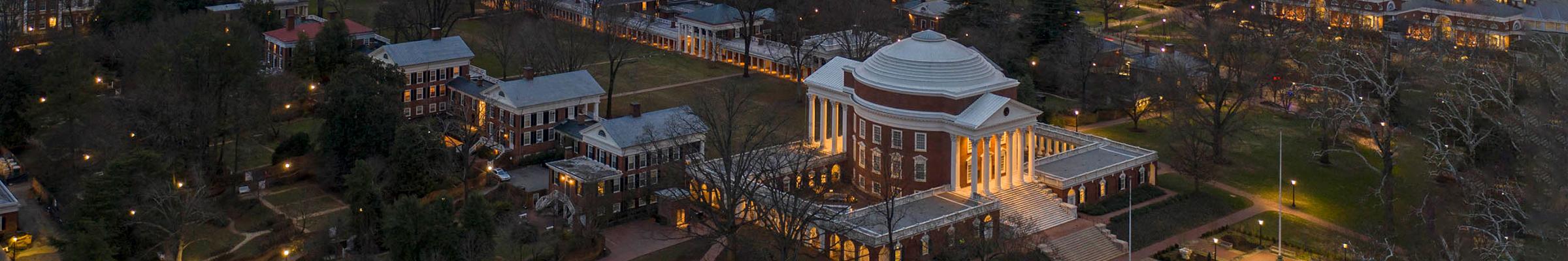 A banner portrait of UVA Lawn from an aerial view, with lights on at dusk.