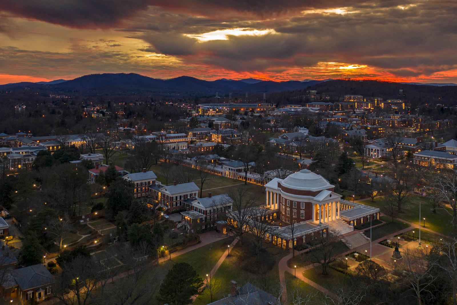 A banner portrait of UVA Lawn from an aerial view, with lights on at dusk.