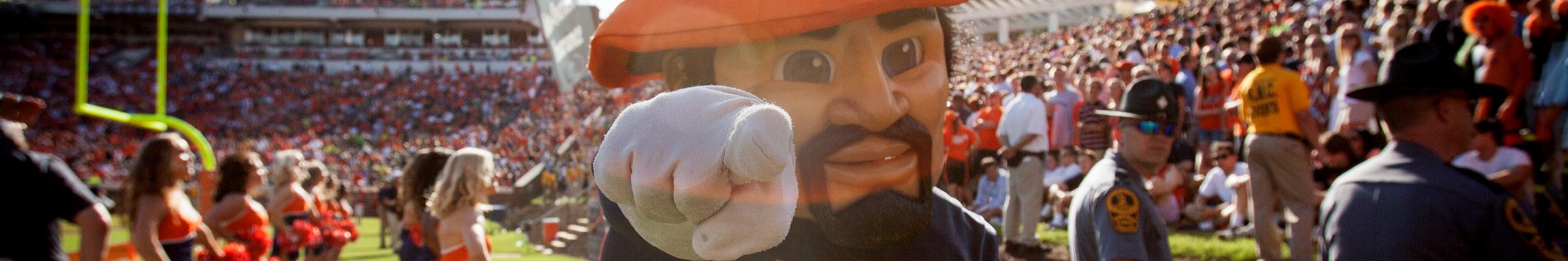 A banner portrait of a UVA Cavman with a large crowd of spectators in the background during game day.